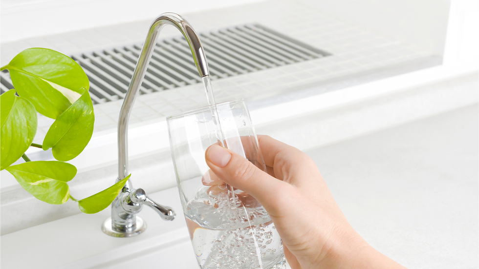 A person holding a glass under a kitchen faucet.
