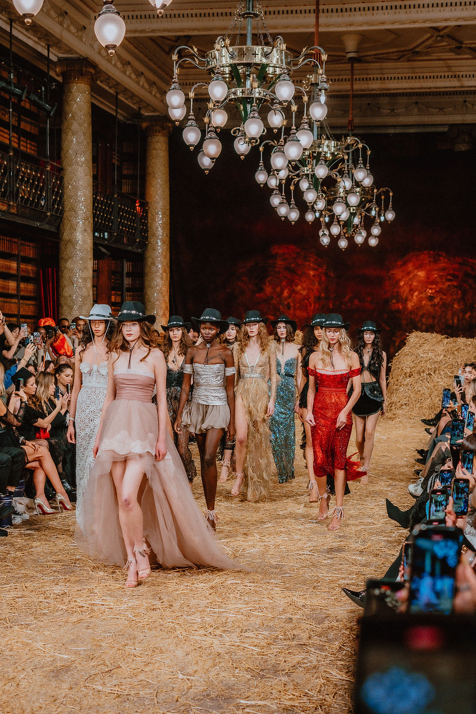 Runway models showcase Aadnevik's A/W 2025 "Western Star" collection, featuring a fusion of rustic elegance and bold glamour, set against a backdrop of opulent chandeliers and rustic hay.