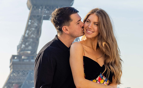 Couple photoshoot at the Eiffel Tower in Paris, man kissing his smiling partner on the cheek