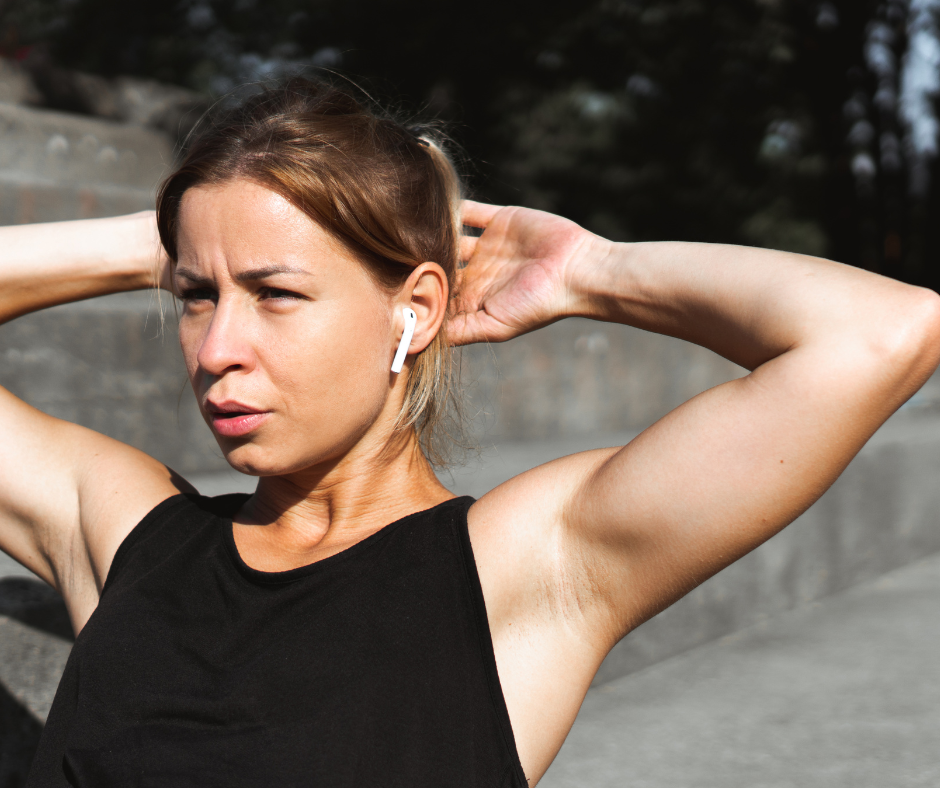 in shape woman holds her hands at her head and breathes out with an air pod in her ear