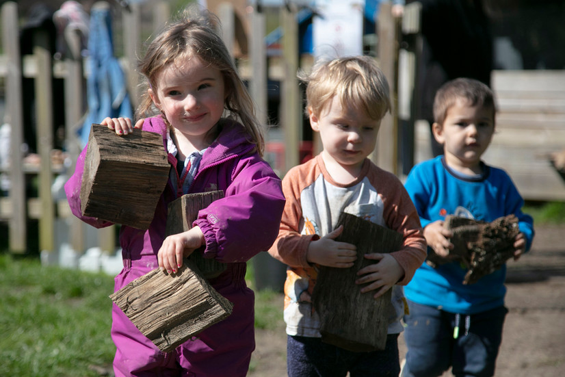 children carrying wood in an outdoor setting.