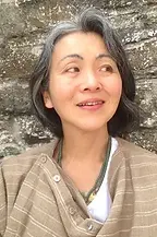 Smiling Asian woman with gray hair and a patterned shawl posing outdoors.