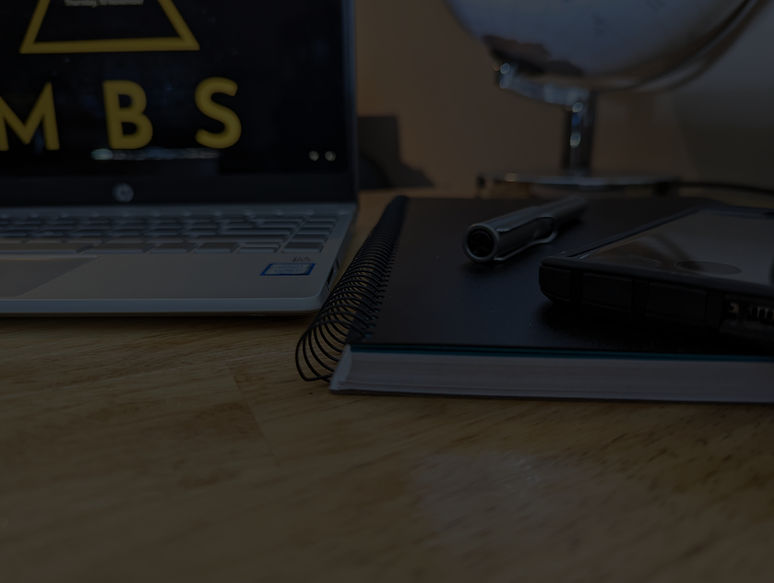 Laptop, notebook, and pen on top of an open book, symbolising learning, planning, and orga