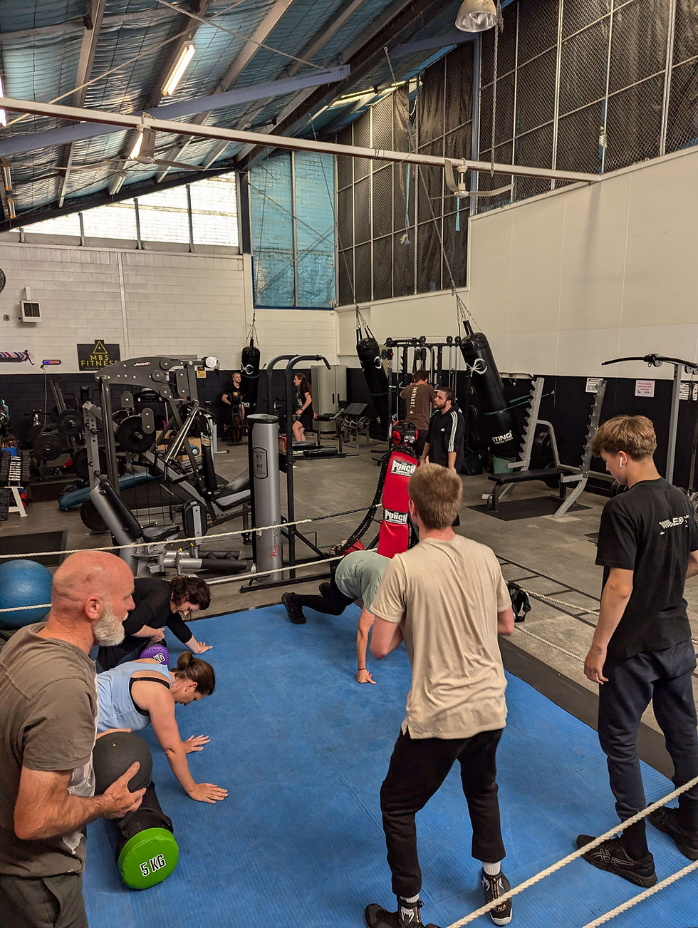 A group of adults training together in a circuit session at MBS Fitness, performing strength and cardio exercises in a supportive environment.