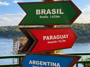 Placas indicando Brasil e Paraguai no Marco das Três Fronteiras, em Foz do Iguaçu, com vista para o encontro dos rios e a paisagem da fronteira.