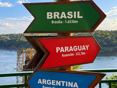 Placas indicando Brasil e Paraguai no Marco das Três Fronteiras, em Foz do Iguaçu, com vista para o encontro dos rios e a paisagem da fronteira.