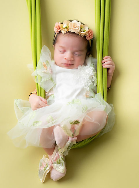 Newborn Photography - newborn baby girl posing on swing and smiling for her luxury newborn photography in newborn dress