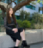 Eirlyse Sollars, founder of Highly Finite, sitting on a ledge outdoors, smiling, with a tree and building behind