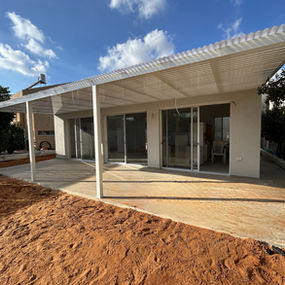 פרגולת אלומיניום בגוון לבן עם כיסוי הצללה של סנטף מסוג BH לאורך ויטרינת היציאה לחצר האחורית בבית פרטי, מבט חזיתי מימין