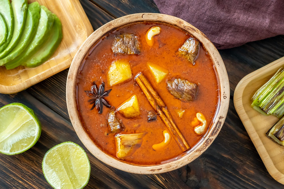 Un bol de curry Massaman thaïlandais avec du bœuf, des pommes de terre, de la cannelle, de la badiane et des noix de cajou, accompagné de citron vert frais et d’aubergines grillées sur une table en bois. Un curry riche en épices, originaire du sud de la Thaïlande avec des influences persanes.
