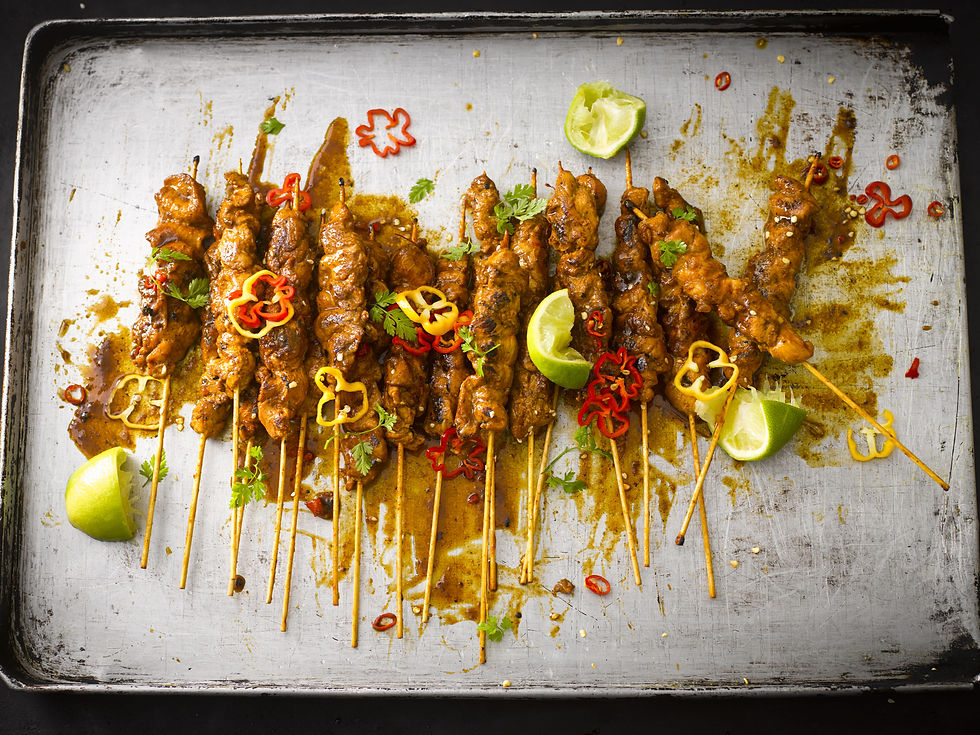 Brochettes de poulet satay nappées de sauce cacahuète pimentée, servies dans une assiette noire avec lait de coco et herbes fraîches.