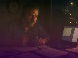Stressed fleet manager working late at night with a headset and coffee, reviewing paperwork next to a laptop showing a truck tracking map.