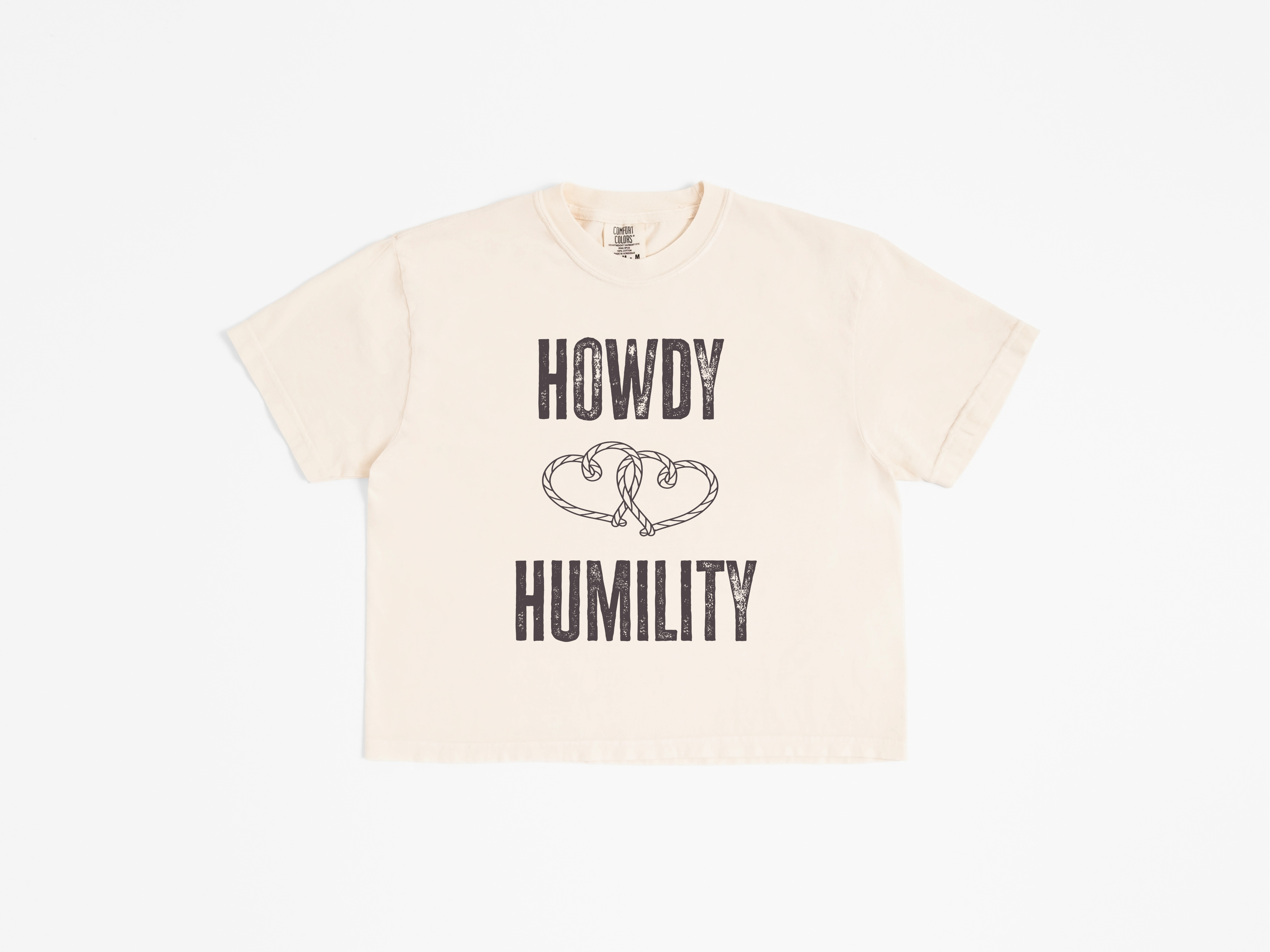 Ivory boxy cropped tee with distressed dark brown "HOWDY HUMILITY" text and two intertwined rope hearts, flat lay front view