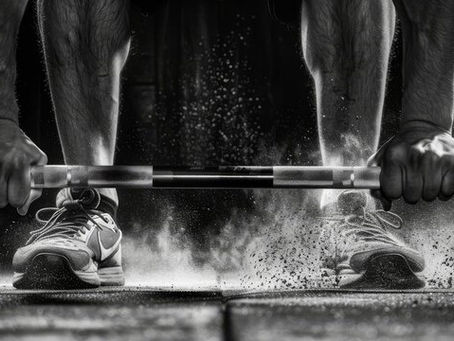 An athlete focuses intensely as they prepare to perform a Romanian Deadlift, gripping the barbell firmly with chalk-covered hands. Dust rises around their steady stance, showcasing a moment of strength and determination.
