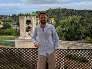 Walter DiLello standing on a terrace overlooking a historic stone bridge and lush countryside in Italy, representing cultural immersion and local perspective.