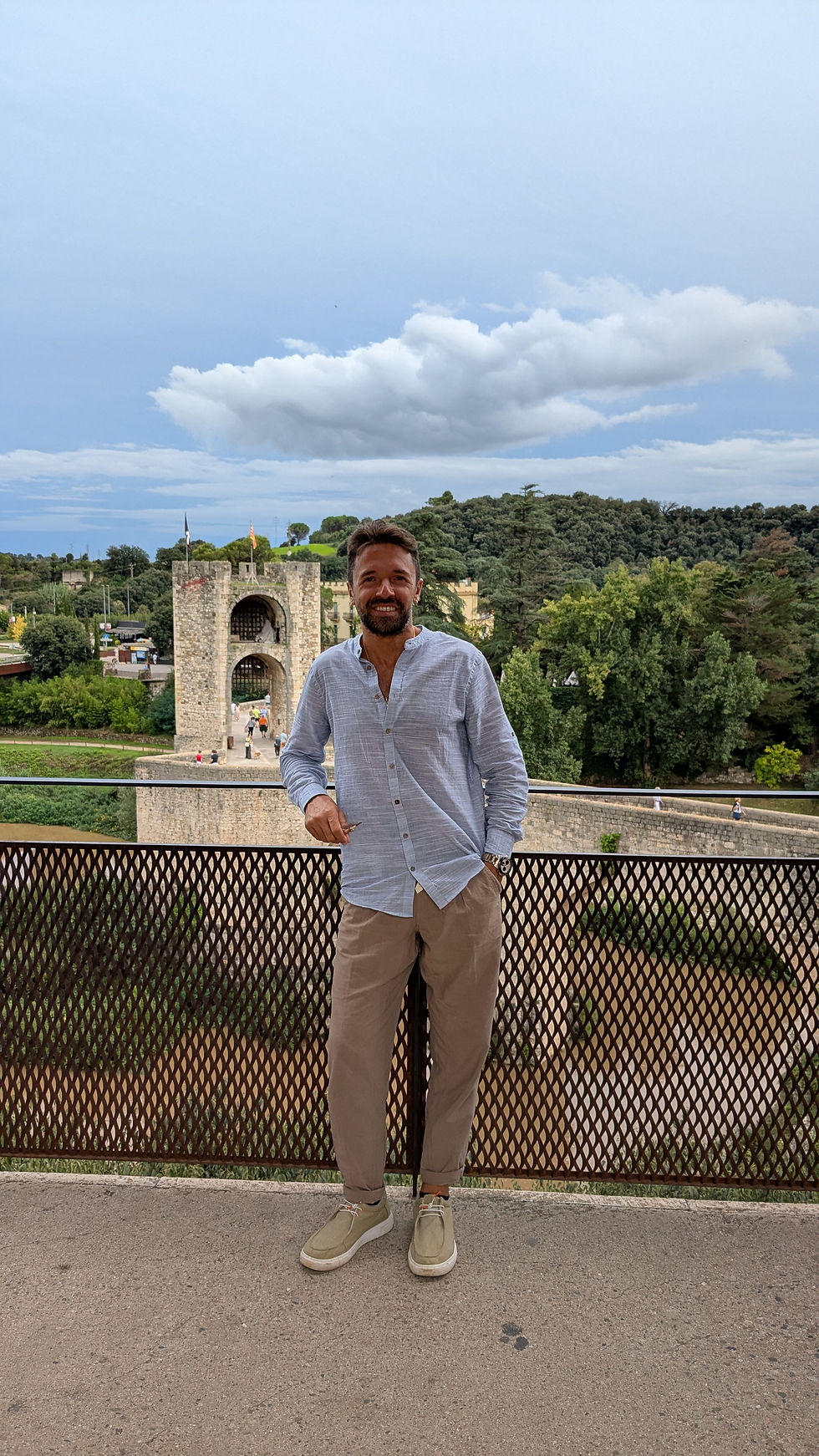 Walter DiLello standing on a terrace overlooking a historic stone bridge and lush countryside in Italy, representing cultural immersion and local perspective.