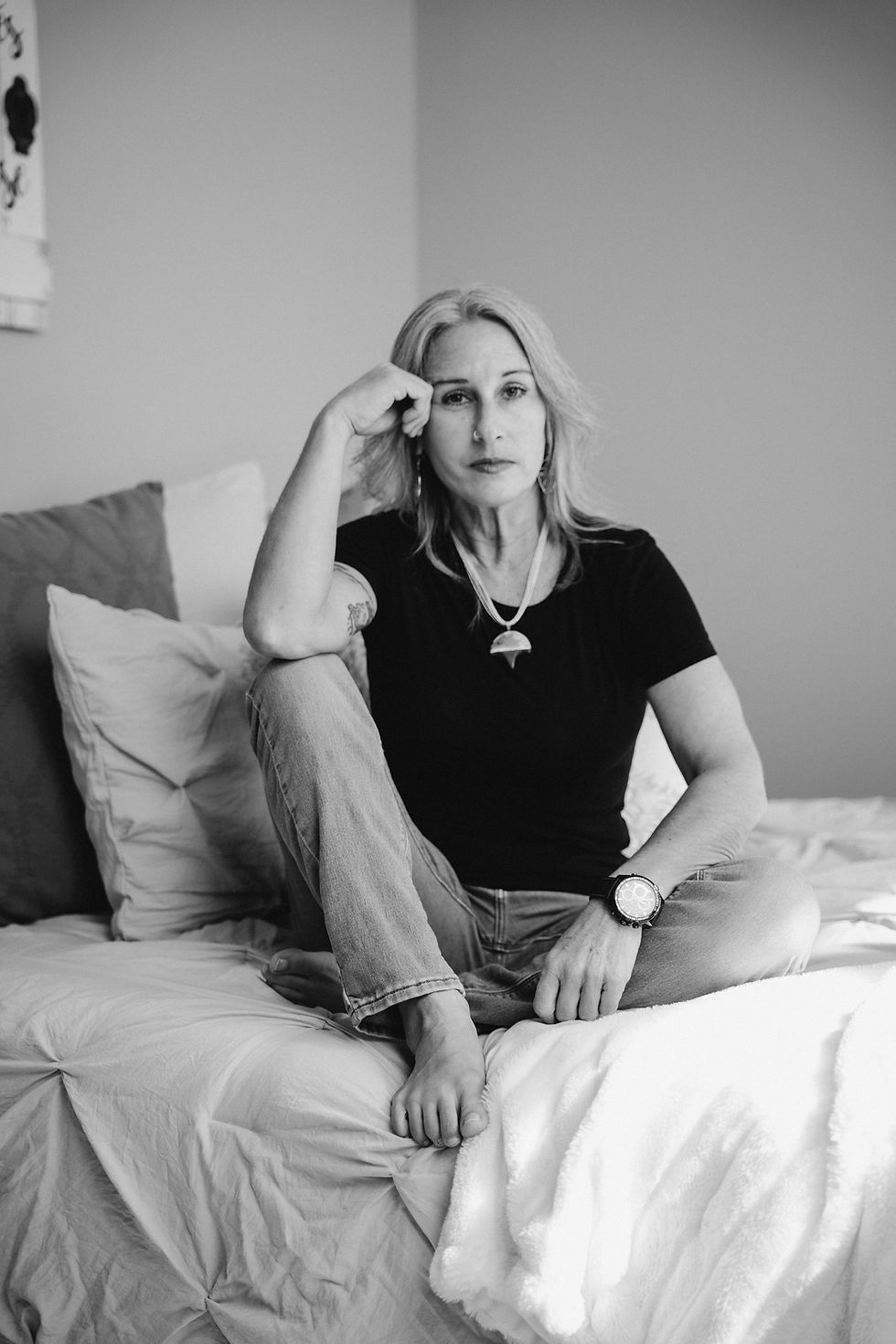Woman sitting thoughtfully on a bed in a quiet space, reflecting on global conflict, humanity, and personal perspective