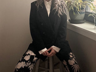 Professional travel outfit featuring a black blazer and patterned trousers styled for comfortable international travel, photographed in natural window light to demonstrate polished yet practical airport fashion.