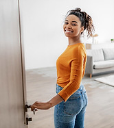 Real Estate. Cheerful African American Female Opening Door Welcoming You To Her New Apartm