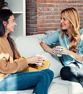 Shot of two smiling young women talking while drinking coffee sitting on couch in the livi