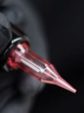 Hand in zwarte handschoen houdt een tatoeage naald cartridge vast met rode inkt.