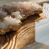 Gold-edged rose quartz and clear quartz geode resting on a reflective golden surface with water reflections and soft lighting for a luxury wellness aesthetic.
