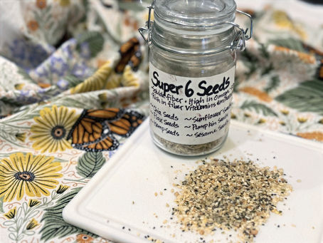 Jar labeled "Super 6 Seeds" with scattered seeds on a white tray. Background features a colorful floral and butterfly patterned fabric.