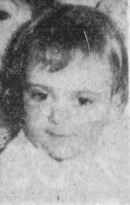 Black and white photo of a content toddler in a white bluse, looking down and to the right.The mood is content.