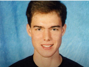 Smiling young adult male with short hair in a colour portrait. The background is blue, creating a warm mood.