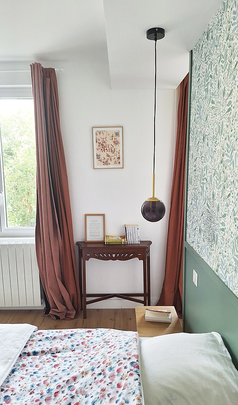 Aménagement et décoration de la chambre parentale avec un papier-peint en t^te de lit, des suspensions en verre fumé et des rideaux terracotta.