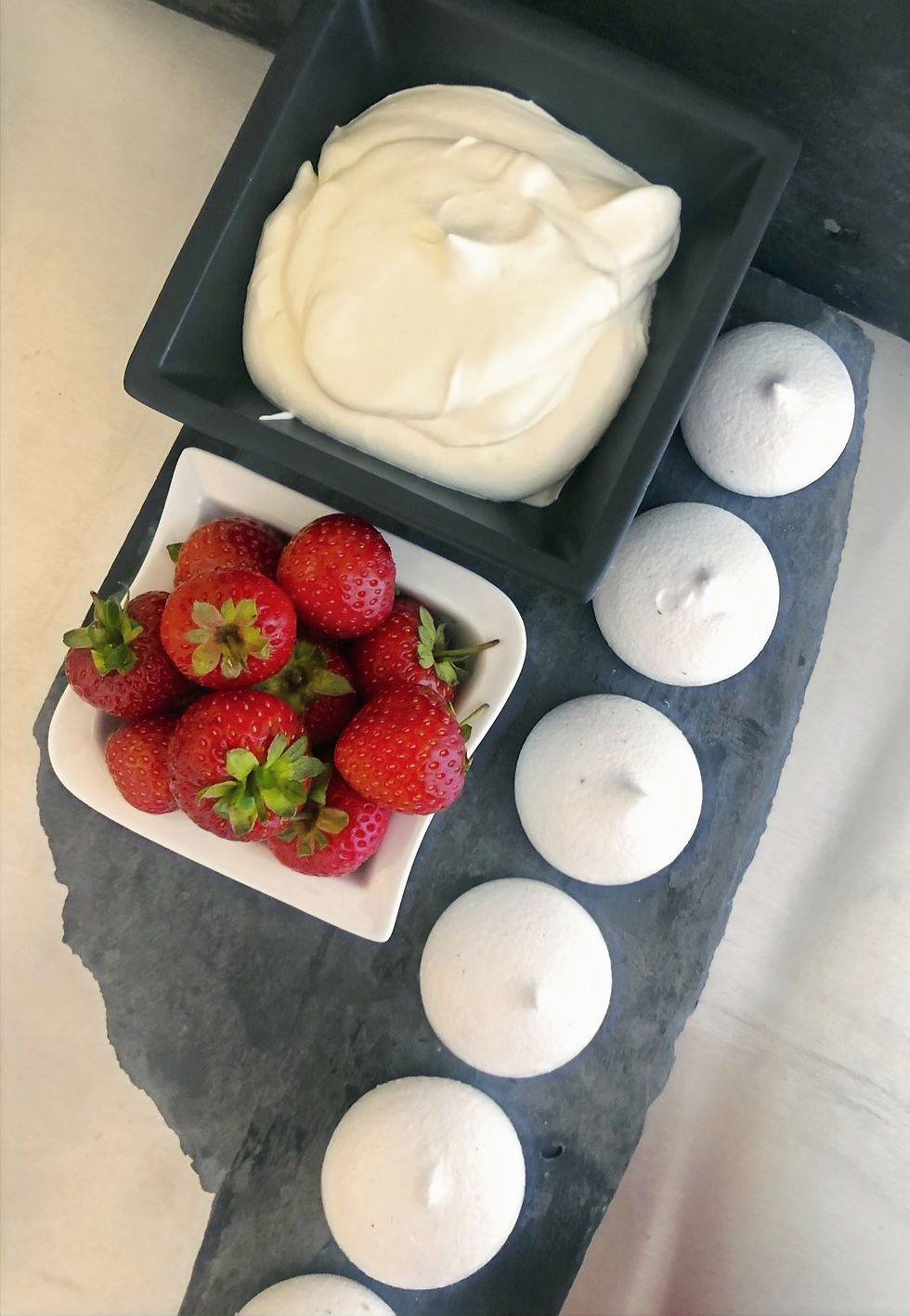 Thumbnail: Bowl of whipped Flora plant cream on slate with a row of Veringue® vegan meringues and fresh strawberries with green calyx