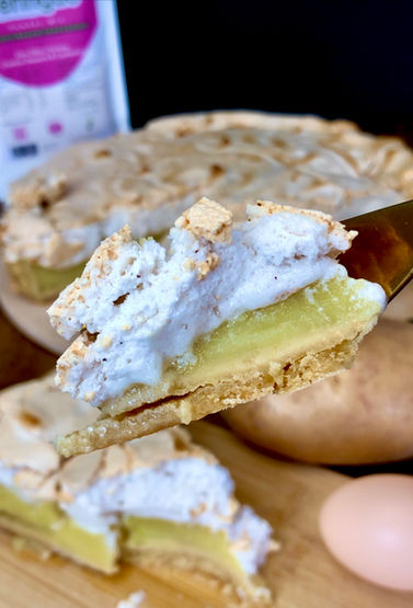 A lush lemon meringue pie showing a close up fork full of pie with a potato in the background