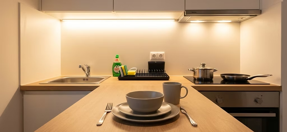 Modern kitchen with wooden countertop, sink, stove with pot and pan. Plates and mugs in the foreground, detergent and sponge nearby.