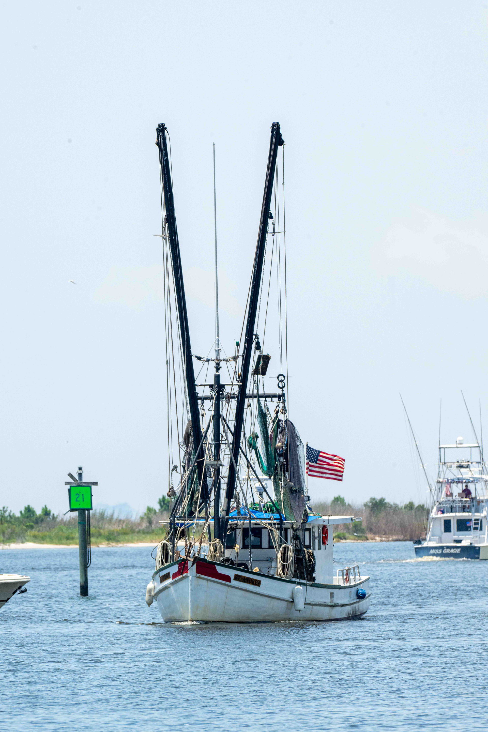 Traditional shrimp boat under clear skies with an American flag, part of the Biloxi Blessing of the Fleet