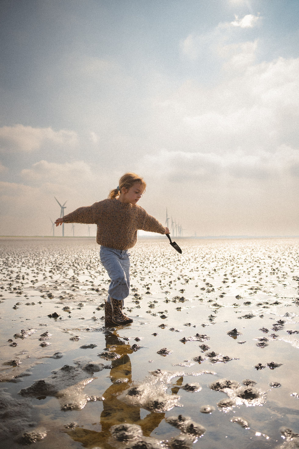 Natuurlijke kinderfotografie Westland – meisje op het strand tussen molens zwaait met haar armen in de wind