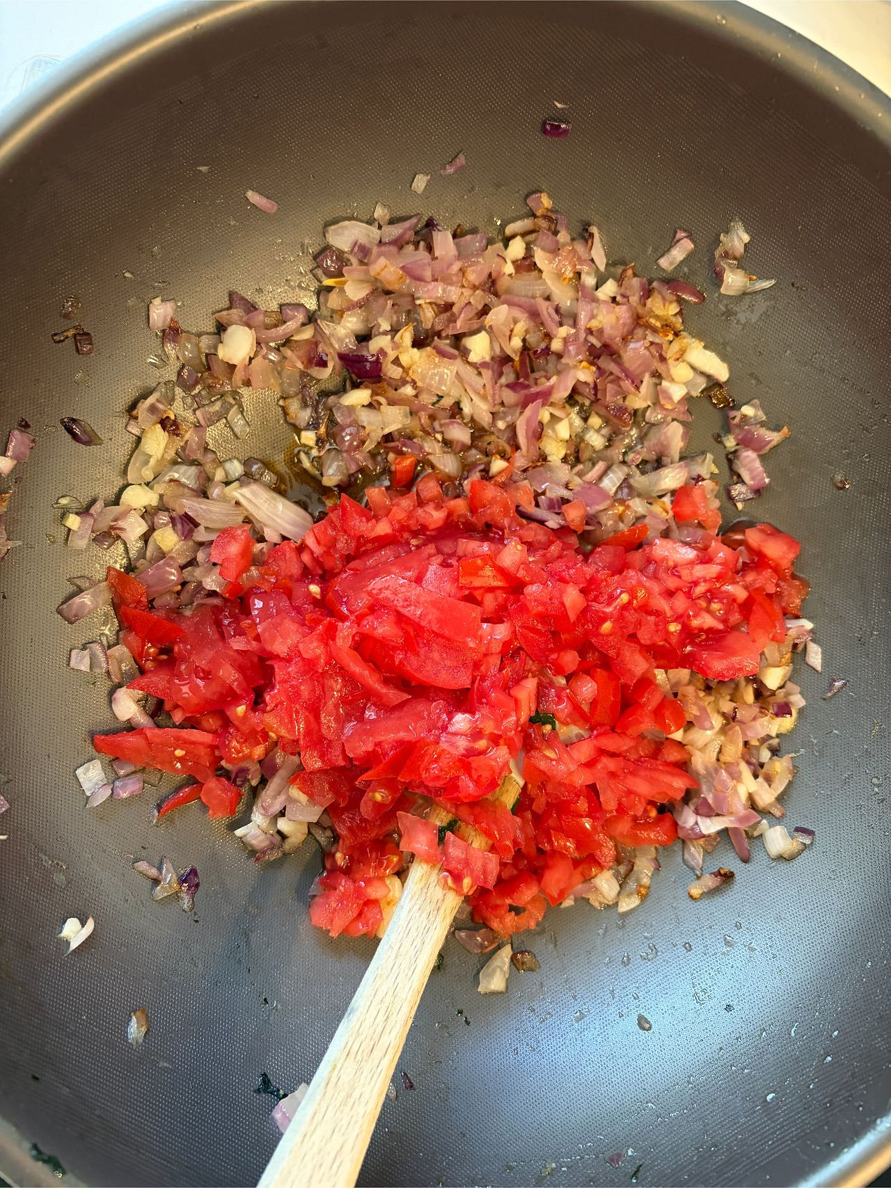 Adding Tomatoes to the Onion and Garlic Mixture for Homemade Palak Paneer Curry