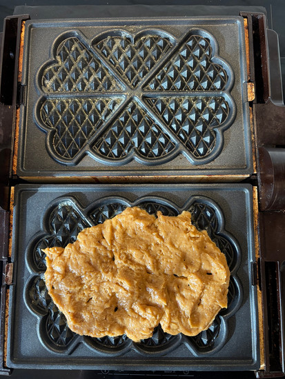 Uncooked brown sourdough waffle batter spread into a heart shaped waffle iron