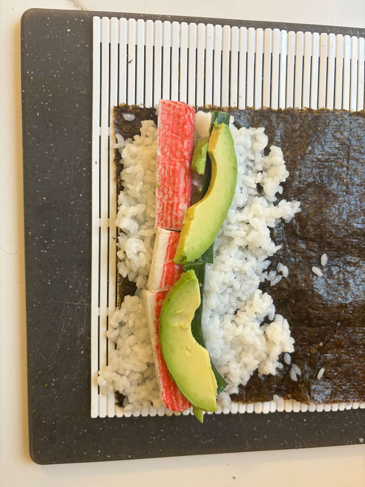 Surimi, cucumber, and avocado placed on sushi rice ready for rolling maki sushi