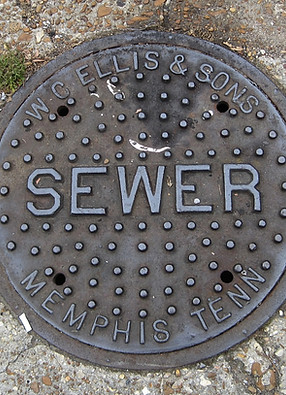 History of the sewer system, depicted by a heavy cast-iron manhole cover featuring the inscription "SEWER" and "MEMPHIS TENN".