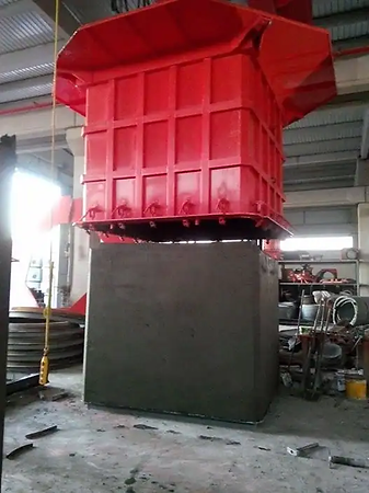 The image shows a freshly cast square/rectangular concrete box culvert or manhole being demolded from a red steel mold inside a plant