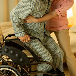Caregiver assisting elderly man into wheelchair