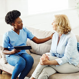A smiling caregiver in a blue uniform comforting an elderly woman in her home