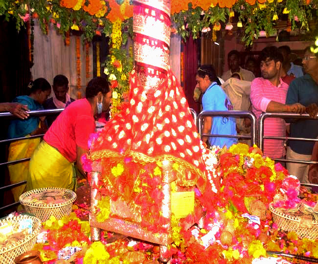 People gather around a colorful, decorated religious altar with flowers and fabrics beneath hanging marigolds, creating a festive atmosphere in Prayagraj kumbh 2025