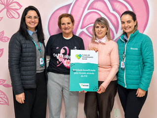 Quatro mulheres sorrindo diante de mural rosa; uma segura placa do Sicoob/FIS com Entidade beneficiada pelo FIS.