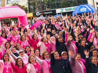 Multidão de mulheres de rosa, sorrindo e erguendo as mãos em evento ao ar livre; faixas D&H Presentes, 2º Tabelião e Sanil.