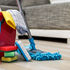 Red cleaning bucket with supplies on the ground with a gray couch behind it