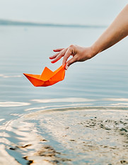 una mano sta poggiando una barchetta di carta sull'acqua