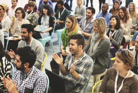an audience of men and women sitting and listening to a speaker, with many clapping