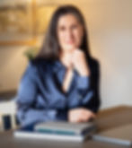 Photo of Sarah Gilbertson sitting at a laptop in a cozy indoor setting, a warm smile, reflecting thoughtful focus and calm confidence.