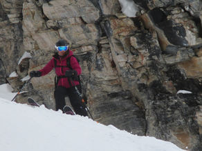 BASI qualified ski instructor Sarah Gilbertson skiing carefully on steep snow near rocky terrain.